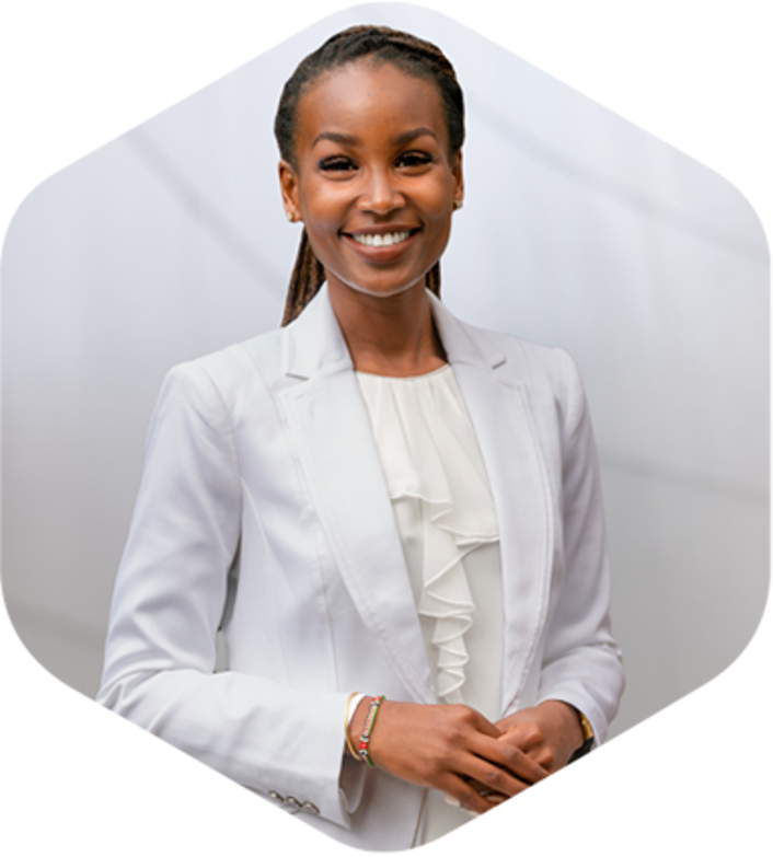 A professional woman in a white suit and tie stands confidently in front of a wall.