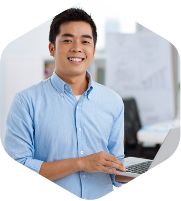 An Asian man in an office, holding a laptop, focused on his work.