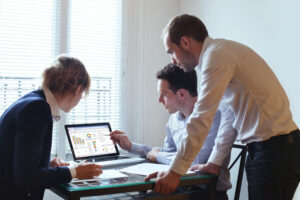 Three people collaborating on a laptop in a professional office setting.